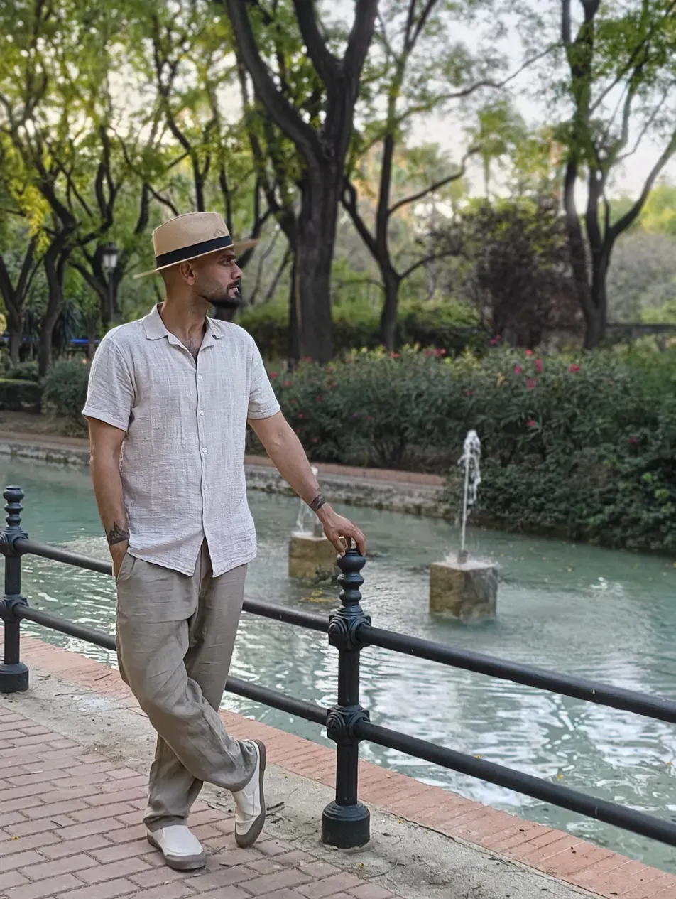 Akhil standing by a park fountain in a hat, looking to distance